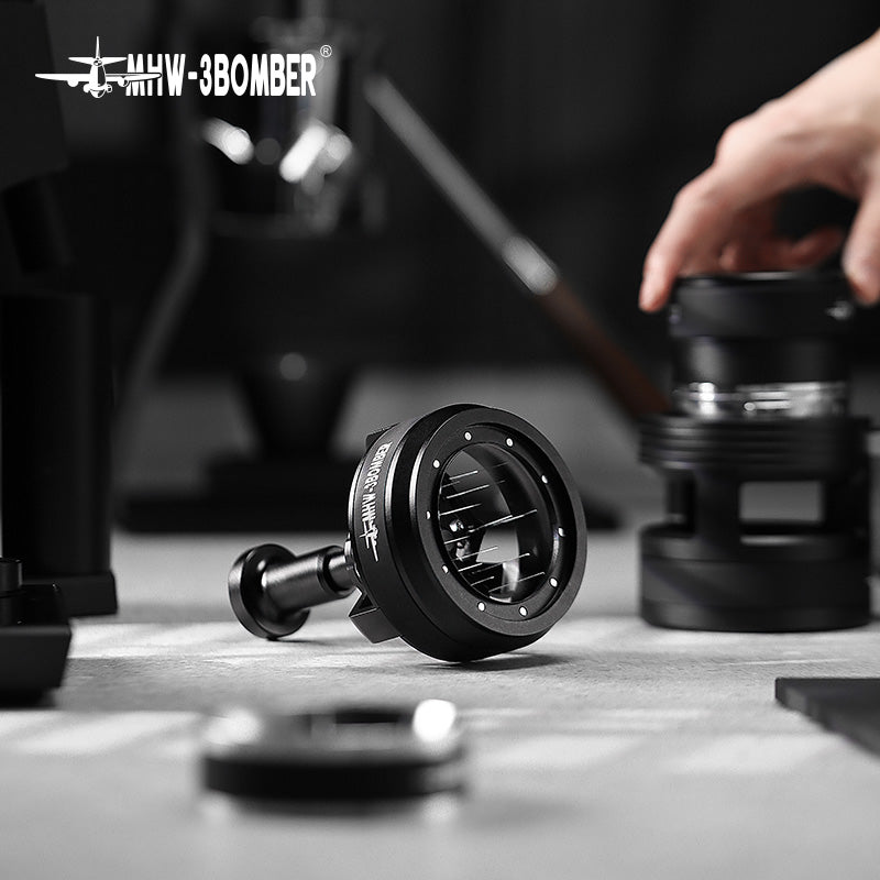 A hand reaches for the MHW-3BOMBER YU Series Cyclone Needle Distributor, set amidst coffee brewing accessories on a gray surface. The focus is on the tool, with a blurred background. MHW-3BOMBER logo appears at the top left.