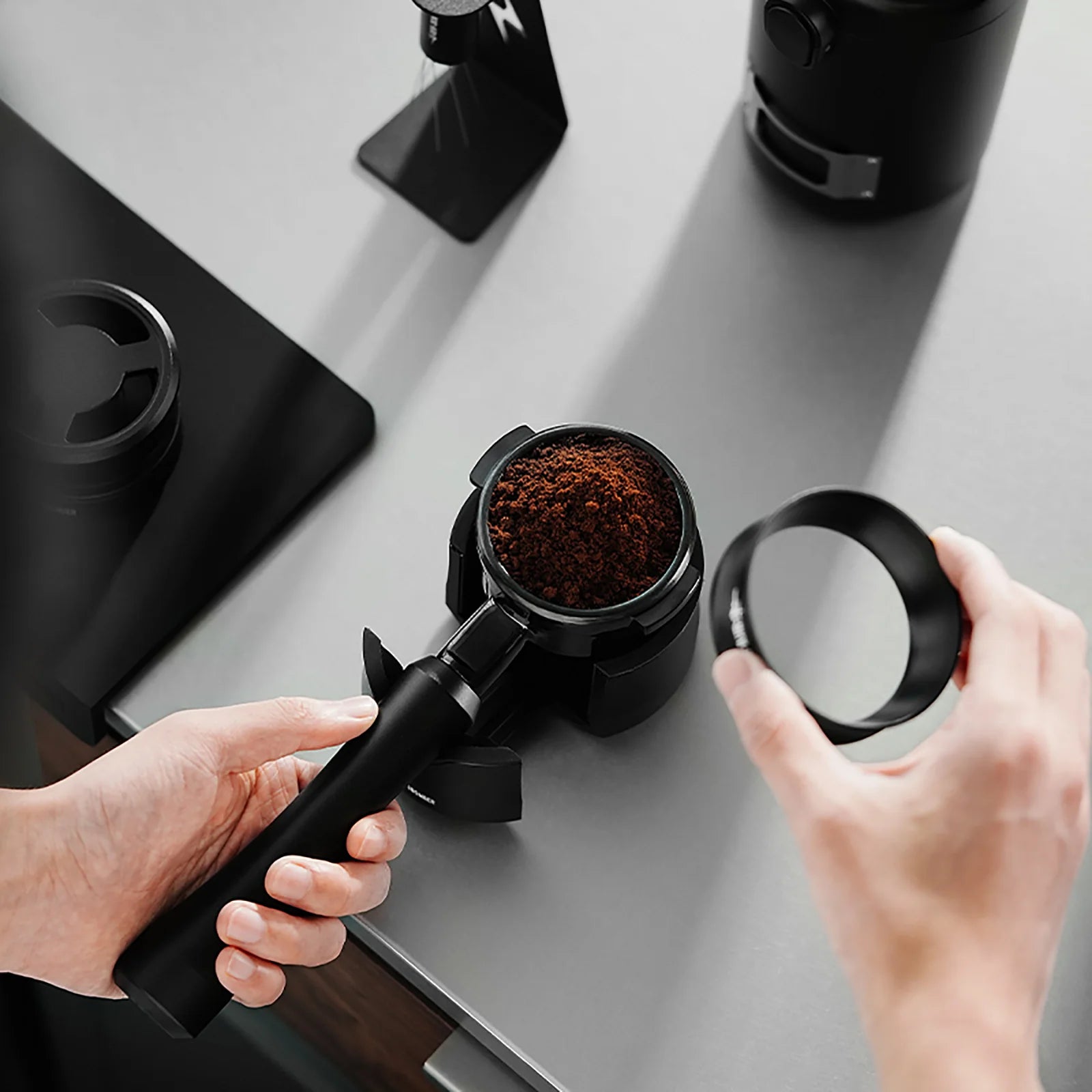 MHW-3BOMBER black bottomless portafilter with coffee grounds being prepared on a counter.