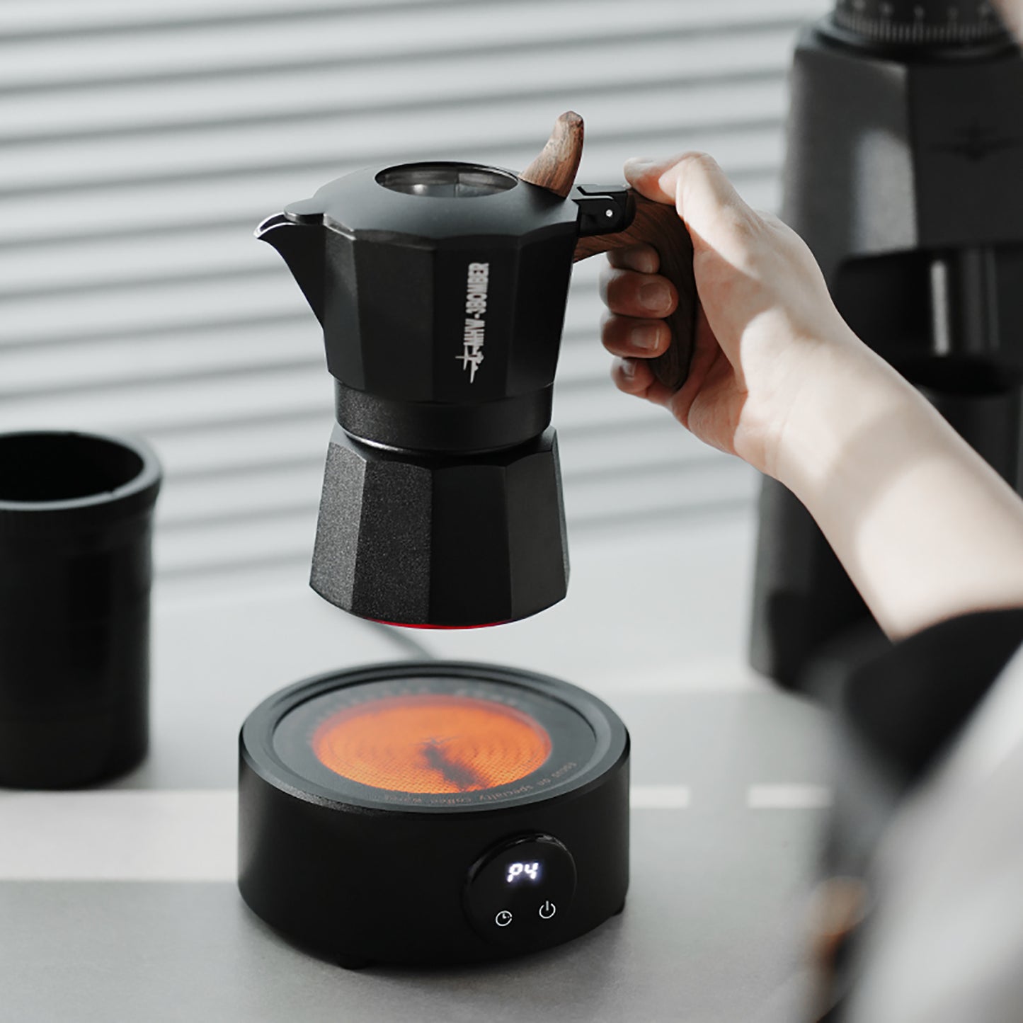 MHW-3BOMBER black moka pot with wood handle on electric coffee heater. Coffee brewing setup.