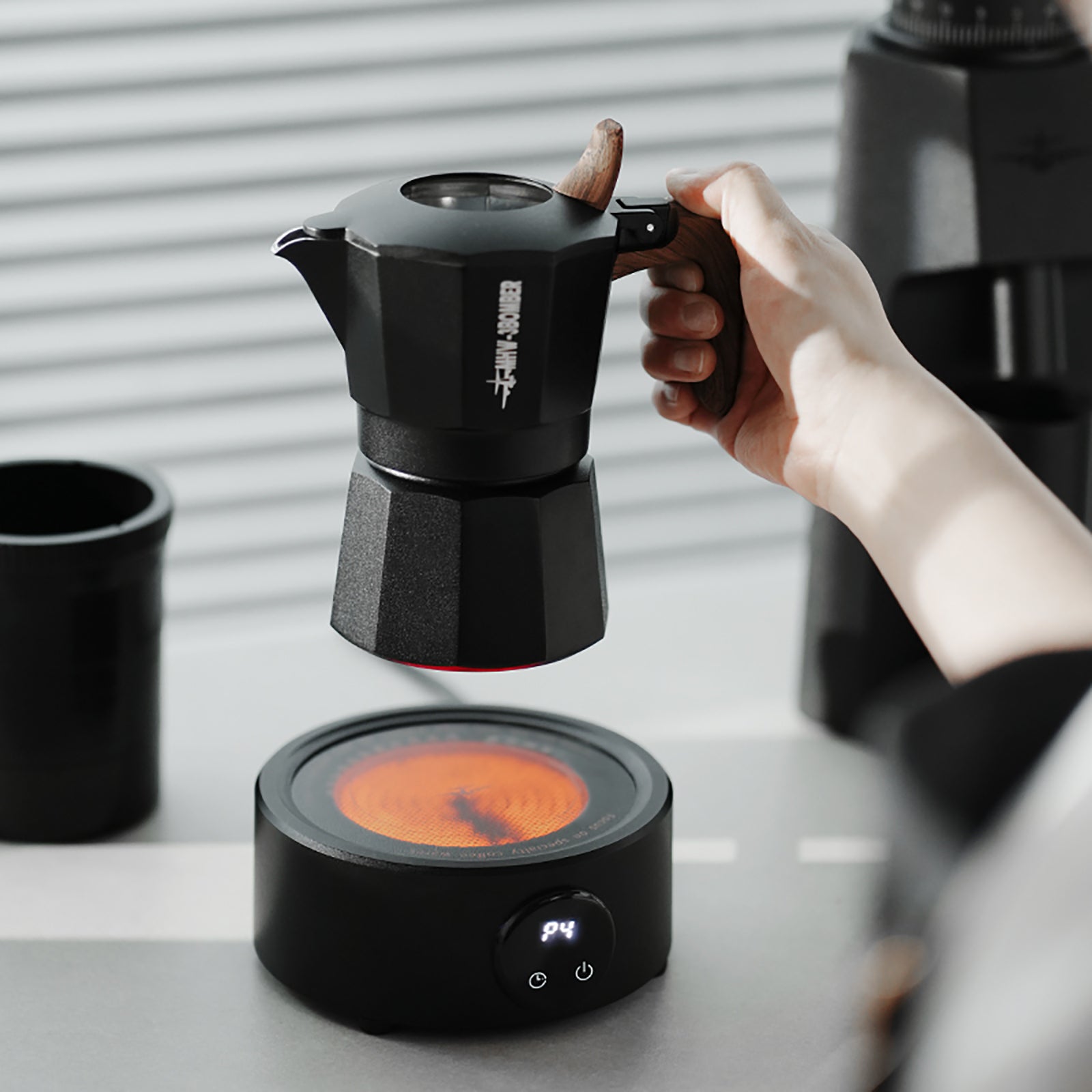 MHW-3BOMBER black moka pot with wood handle on electric coffee heater. Coffee brewing setup.
