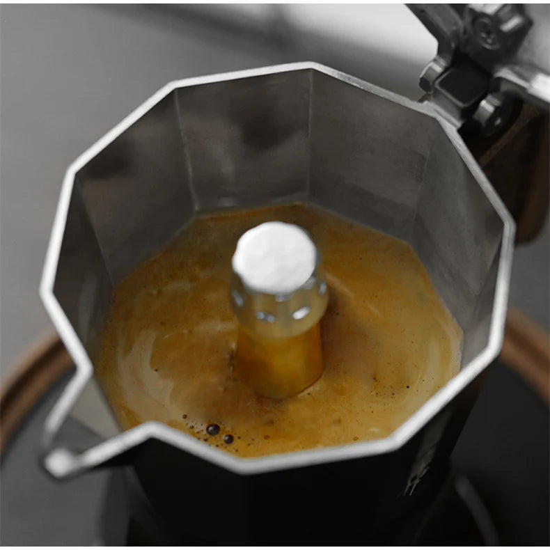 Close-up of brewing with the MHW-3BOMBER Double Valve Moka Pot 100ml; its durable design ensures rich, golden-brown coffee bubbles beautifully in the chamber. The lid is slightly open, inviting you to savor the experience.