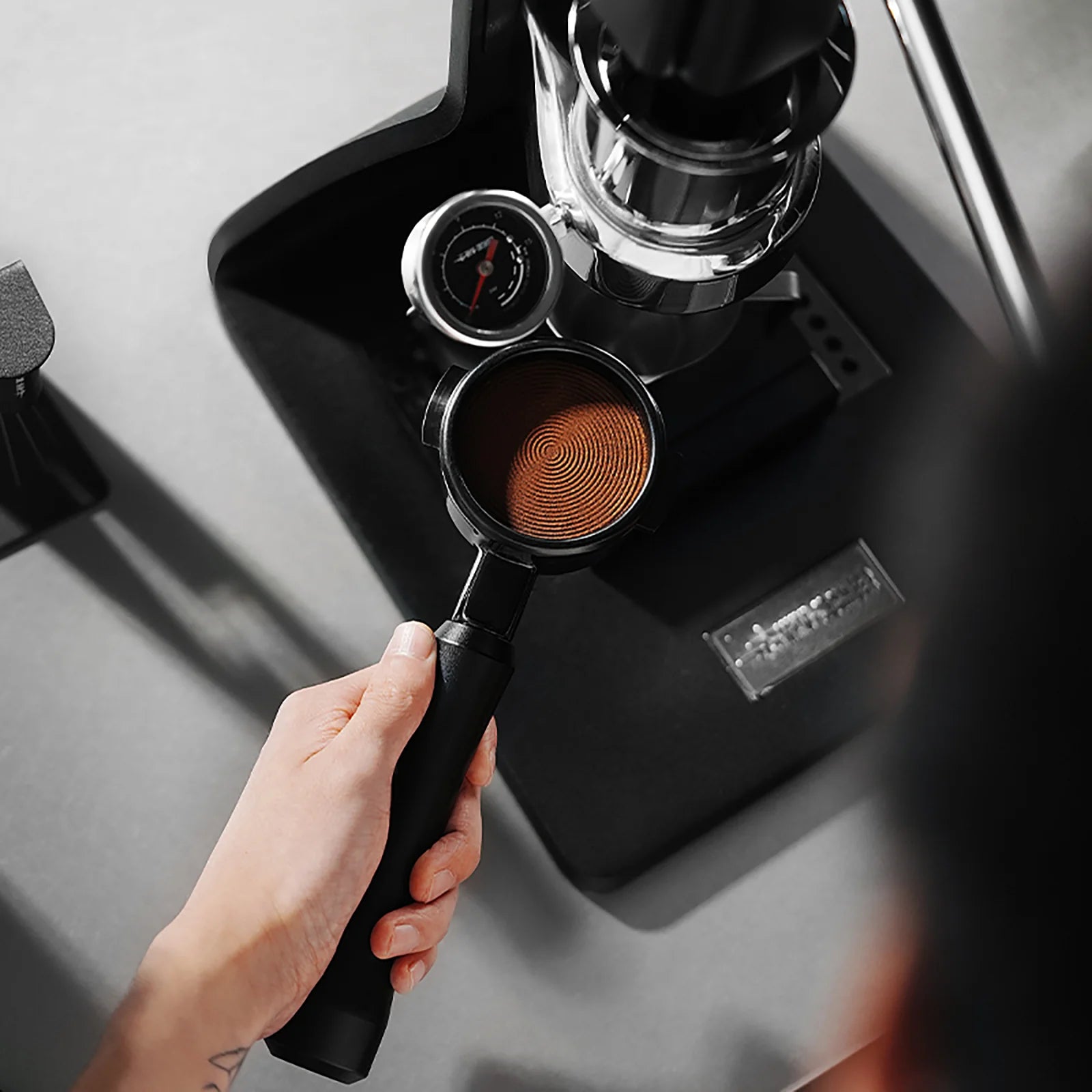 MHW-3BOMBER Astra portafilter filled with ground coffee being attached to a black espresso machine.