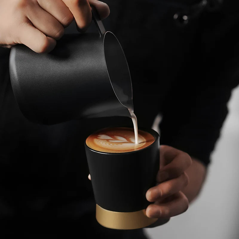 MHW-3BOMBER CERA Black ceramic cup being filled with milk; showcasing U-shaped design and color-blocking metal base.