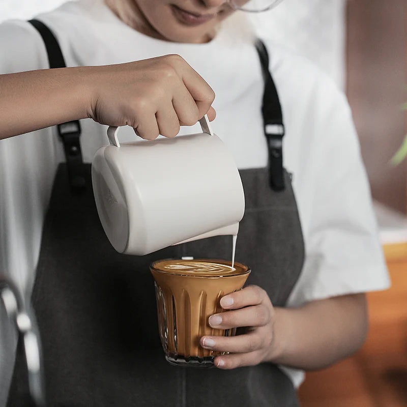 MHW-3BOMBER GT Milk Pitcher glossy, white, being used to pour milk into a glass of coffee.