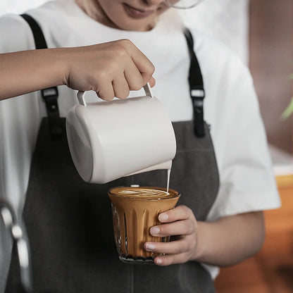 MHW-3BOMBER GT Milk Pitcher glossy, white, being used to pour milk into a glass of coffee.