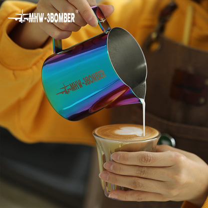 A person in a yellow shirt and apron expertly pours milk from a MHW-3BOMBER Latte Art Pitcher 5.0 Colorful, adorned with a crocodile spout and an airplane logo, into a glass of coffee, creating latte art.