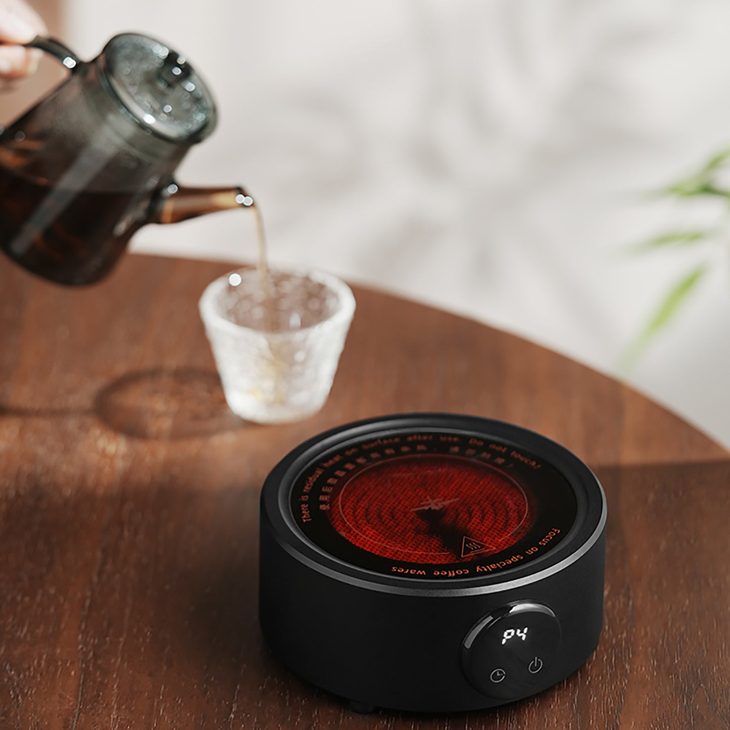 MHW-3BOMBER electric coffee heater in black. Hot plate shown, pouring water in glass. Compact, adjustable temp.