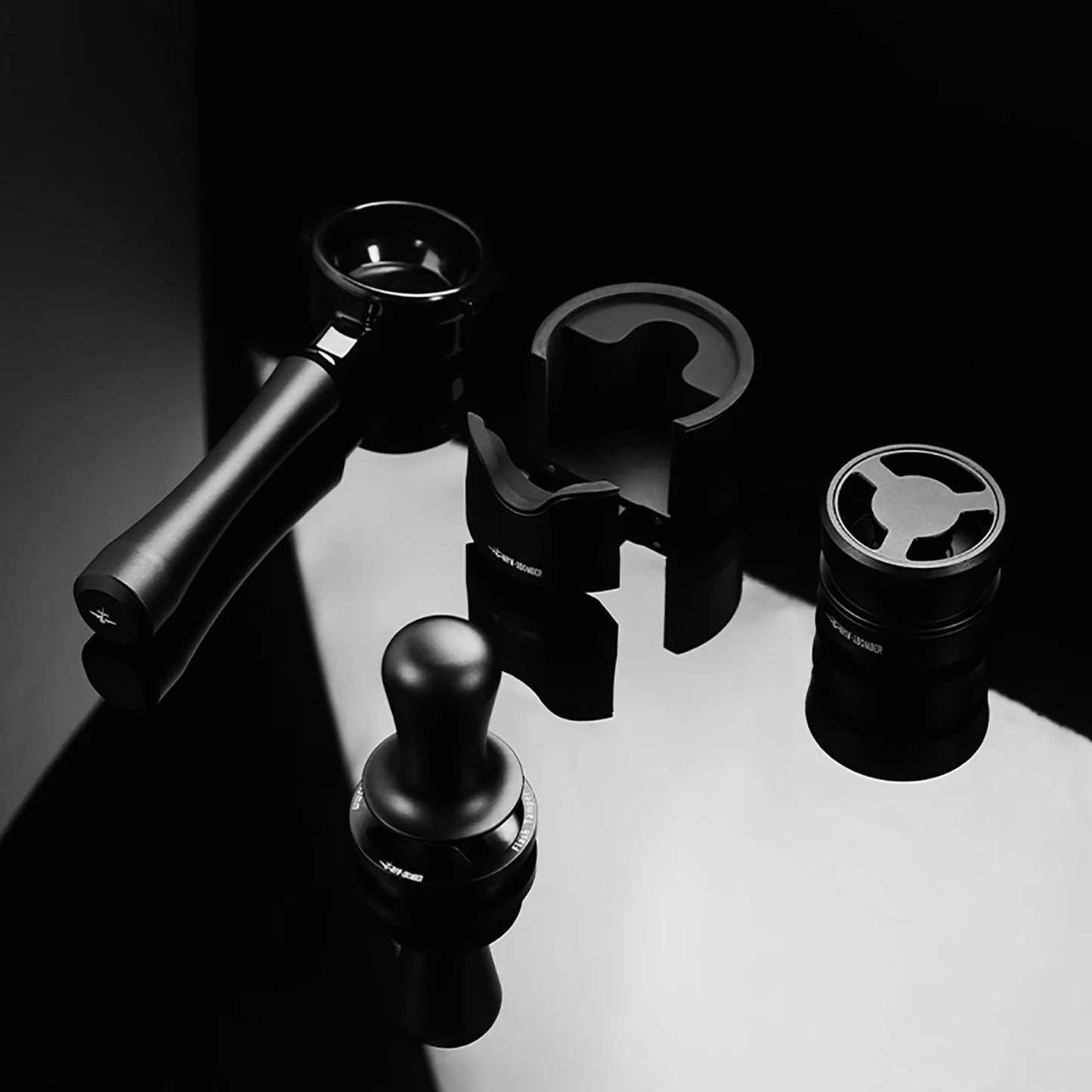 MHW-3BOMBER Astra Collection espresso accessories: bottomless portafilter, tamper, and stand in black.