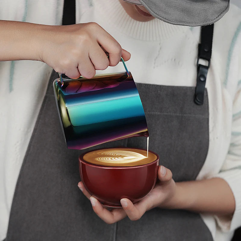 MHW-3BOMBER GT milk pitcher, pouring milk into a red cup. Glossy, rainbow finish, latte art in progress.