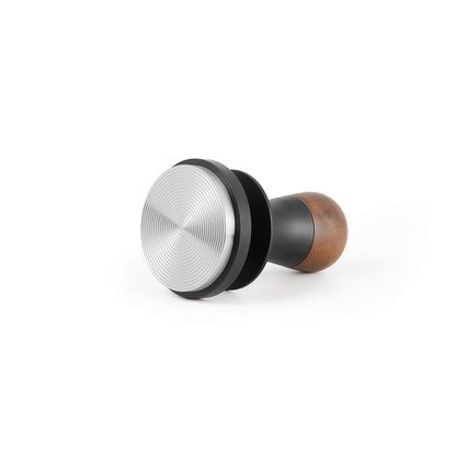 The MHW-3BOMBER Flash Tamper 2.0 features a ridged base and ergonomic wooden handle, offering a sleek metal design that sits elegantly on a white backdrop. Ideal for coffee enthusiasts seeking precision with style, it provides 30lbs of constant pressure and sound feedback.