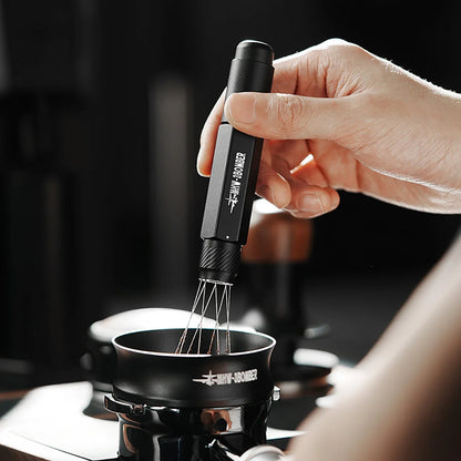 A hand holds the sleek MHW-3BOMBER Lightning Needle Distributor Pro WDT Tool above a small black pot on the stovetop. The contrast of its dark handle and stainless steel design complements any kitchen setup, while the blurred background highlights its efficient performance.