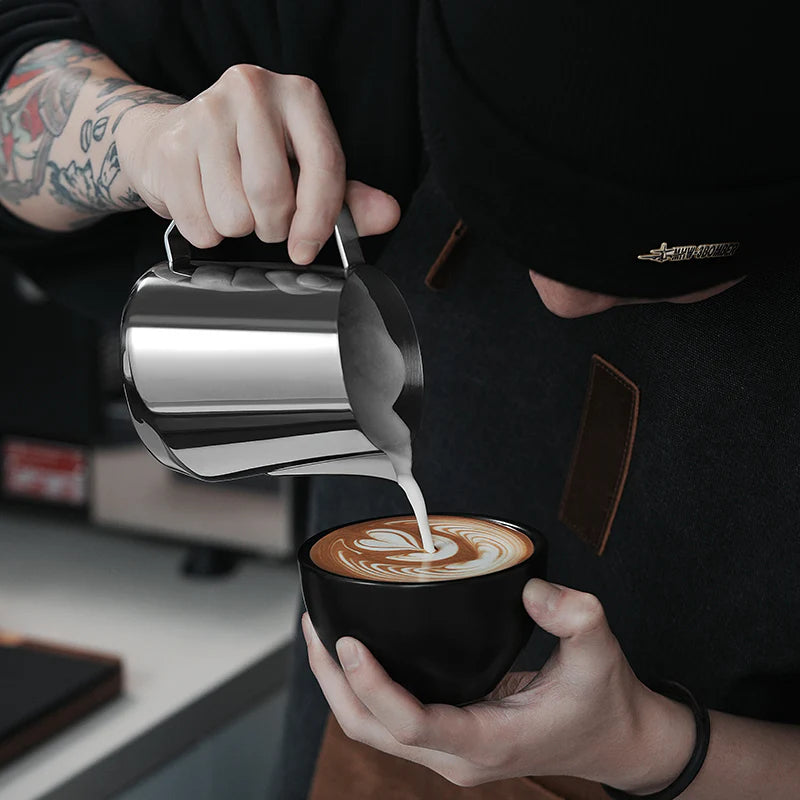 MHW-3BOMBER GT Milk Pitcher being used to pour latte art. Stainless steel with u-shaped spout.