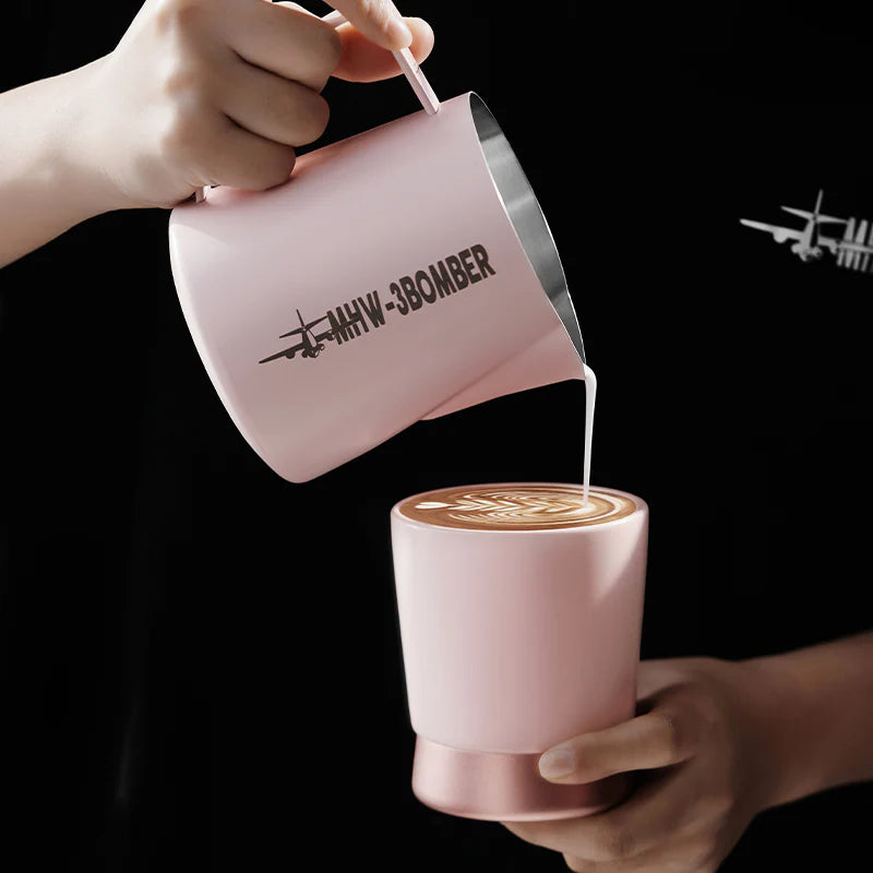MHW-3BOMBER pink milk pitcher pouring into a pink CERA ceramic cup. Latte art visible. Airplane logo detail on pitcher.