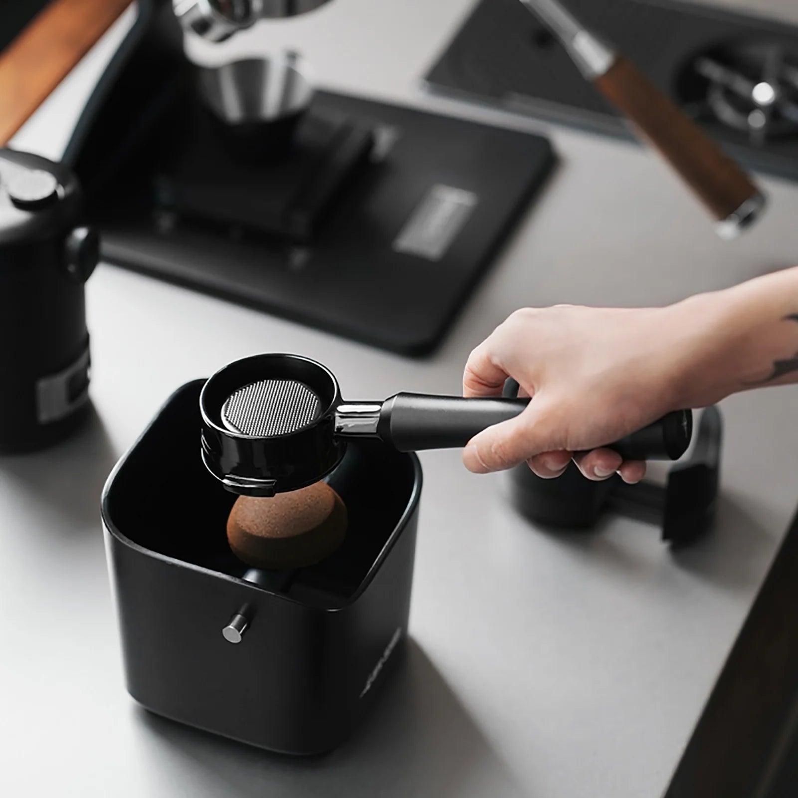 MHW-3BOMBER black Astra portafilter being used with a tamper, on counter. 
