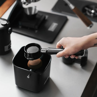 MHW-3BOMBER black Astra portafilter being used with a tamper, on counter. 