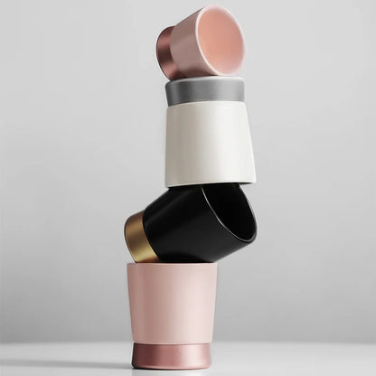 Stacked MHW-3BOMBER CERA ceramic cups in pink, black, white, gray with color-blocked metal bases. Modern design.