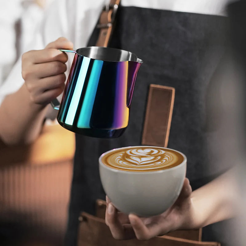 MHW-3BOMBER GT milk pitcher with rainbow finish pouring latte art into cup. Glossy, steel milk frothing pitcher in use.
