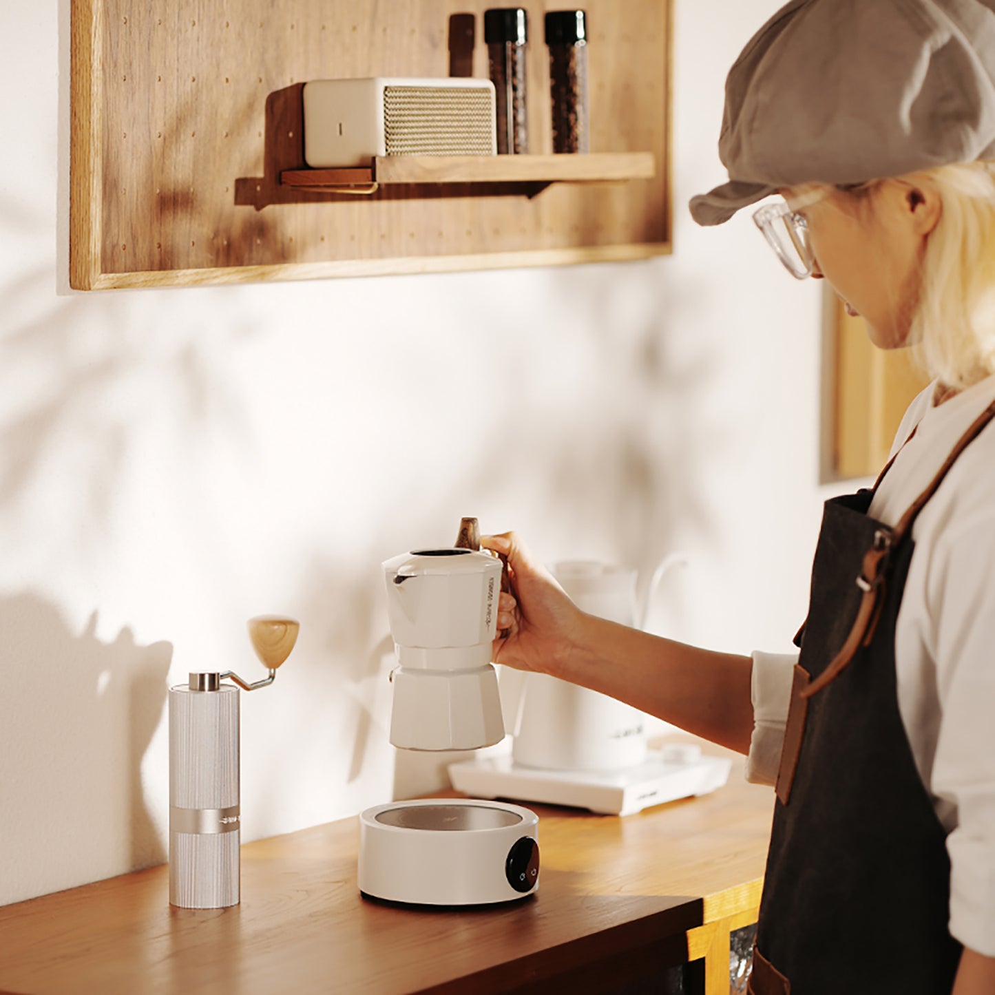 MHW-3BOMBER white electric coffee heater with moka pot and grinder on a counter. 