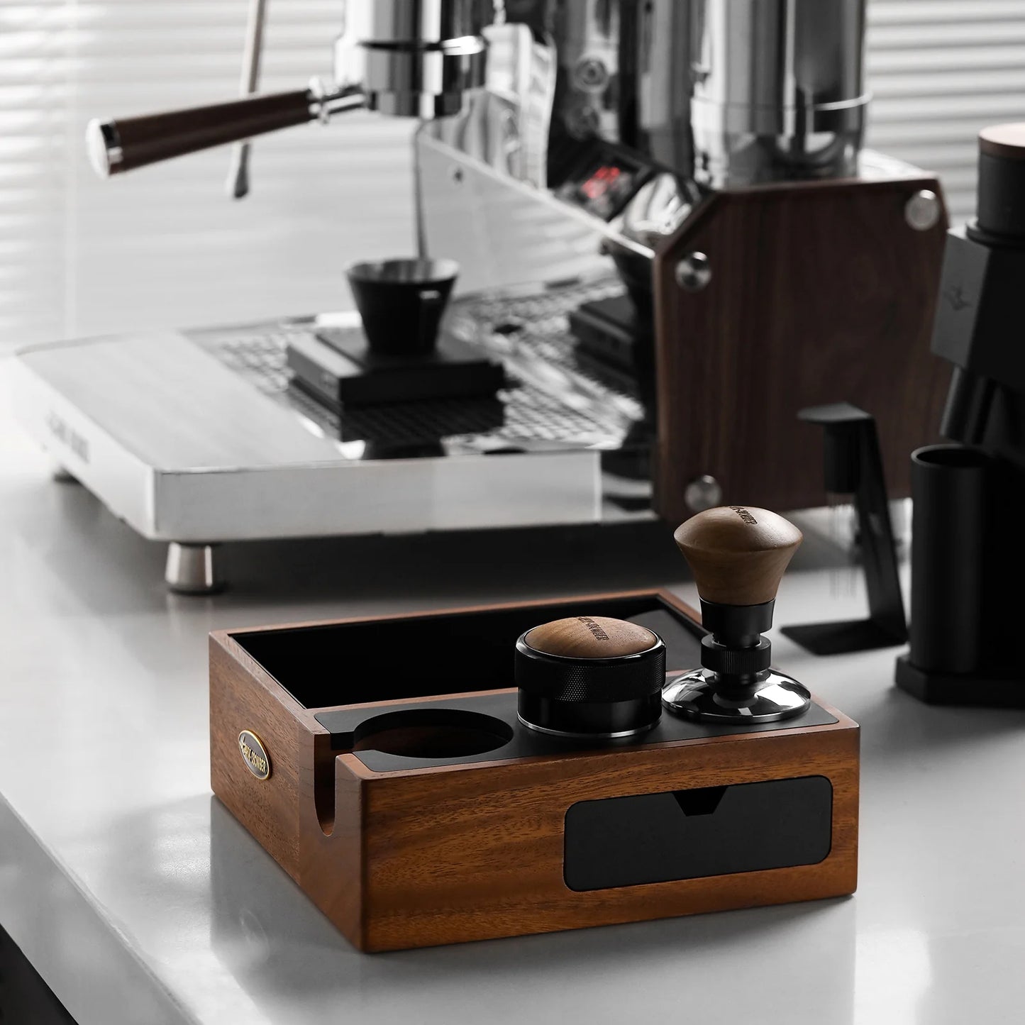 MHW-3BOMBER espresso knock box, walnut wood with black drawer, tamper and coffee distributor on counter. 
