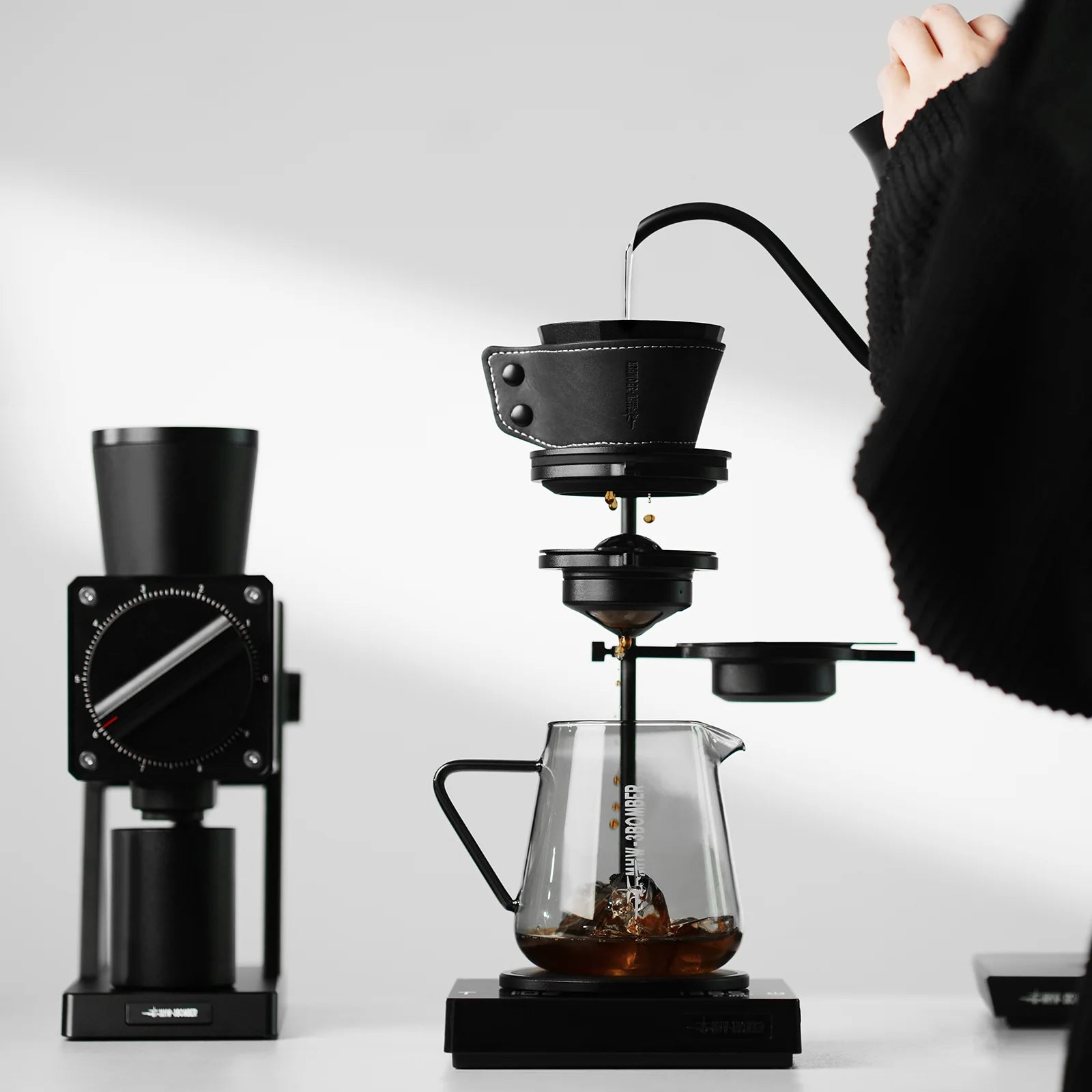 Brew Starter Kit: Black coffee grinder, dripper with leather sleeve, and clear glass server. Pour-over setup.