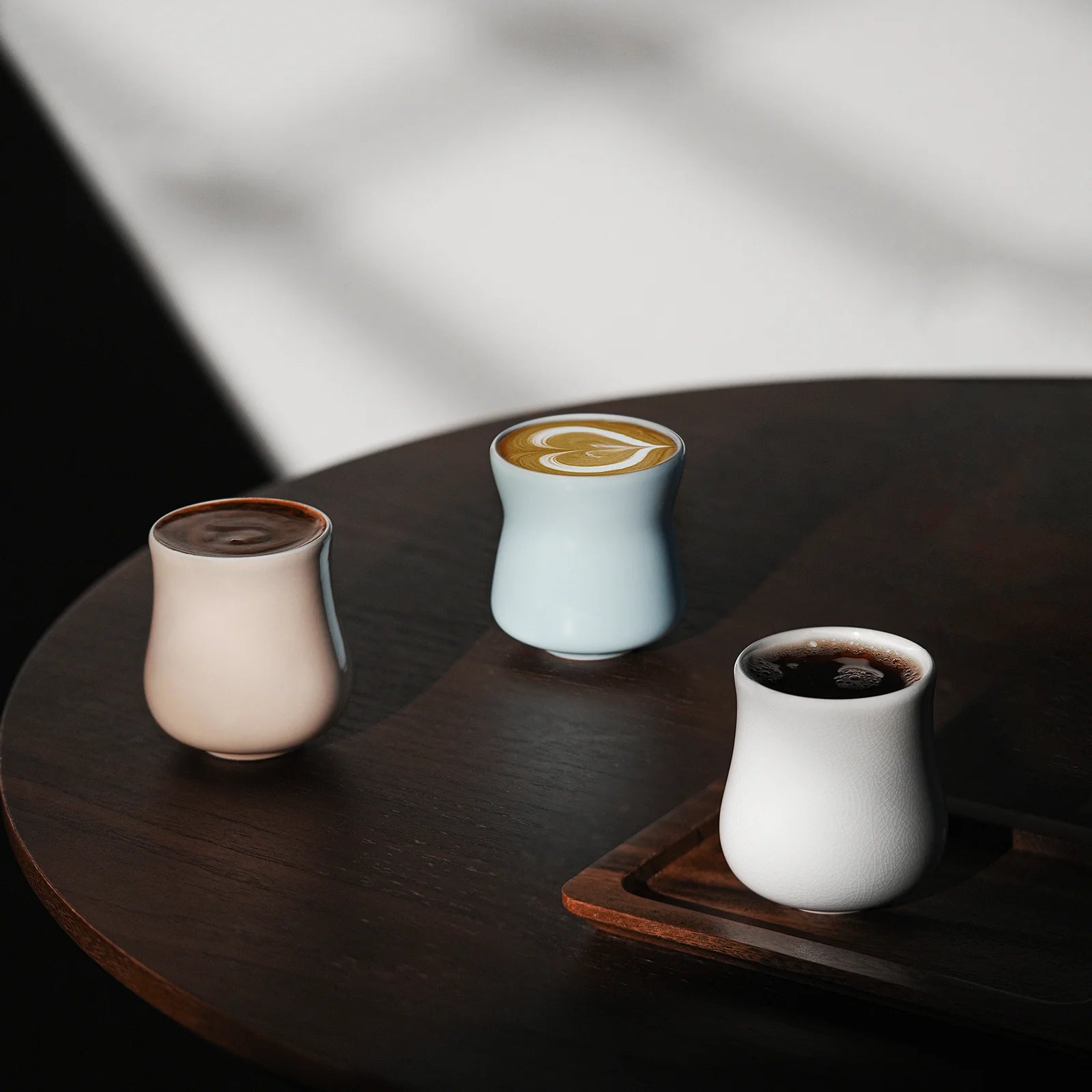 MHW-3BOMBER Aura cups: ceramic, unique shapes, pink, blue & white, filled w/ coffee on wood table. 