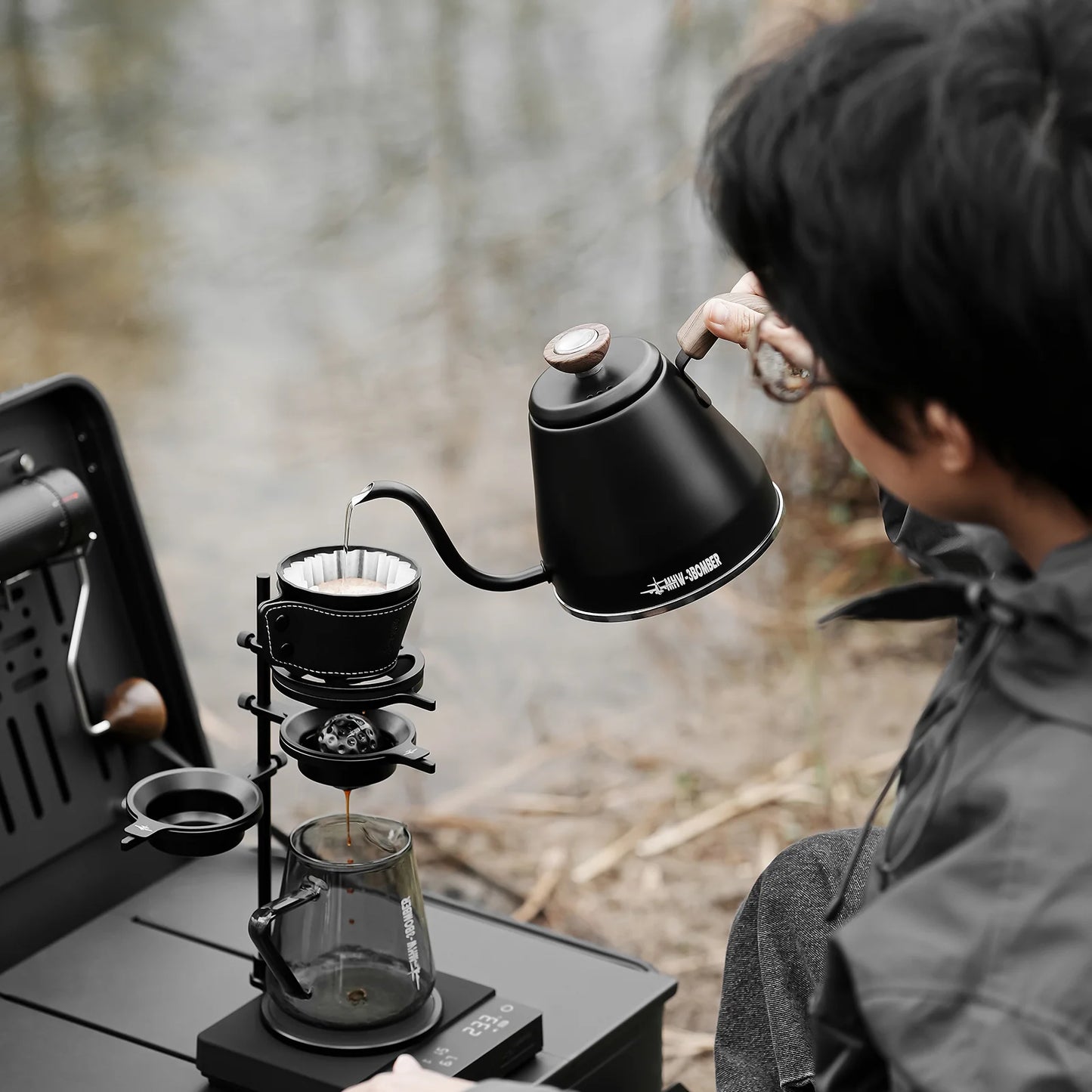 Brew Starter Kit: Pouring hot water from a black kettle into a dripper over a glass server, outdoors.