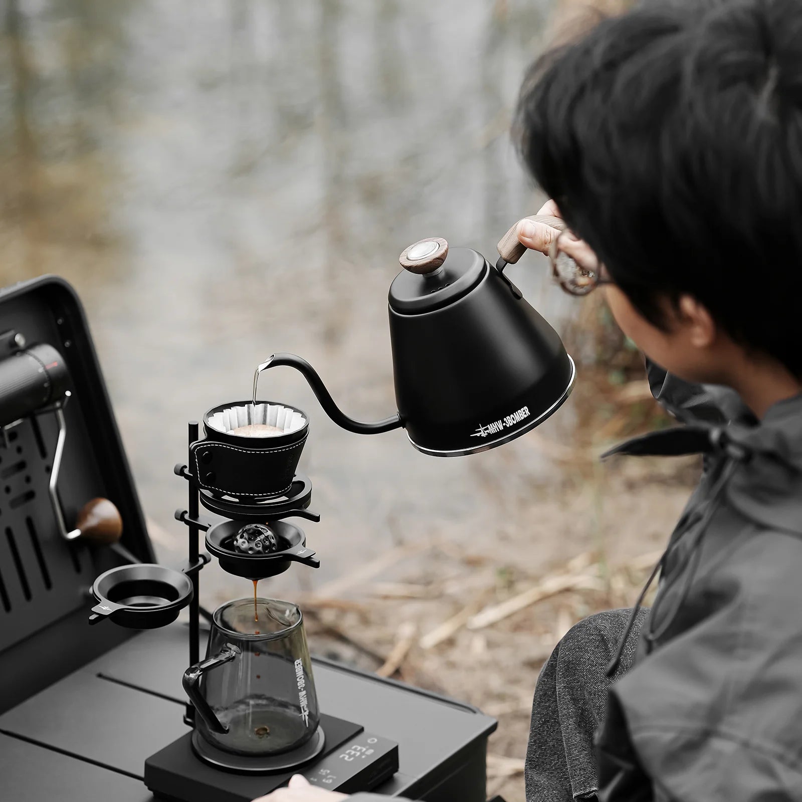 Brew Starter Kit: Pouring hot water from a black kettle into a dripper over a glass server, outdoors.