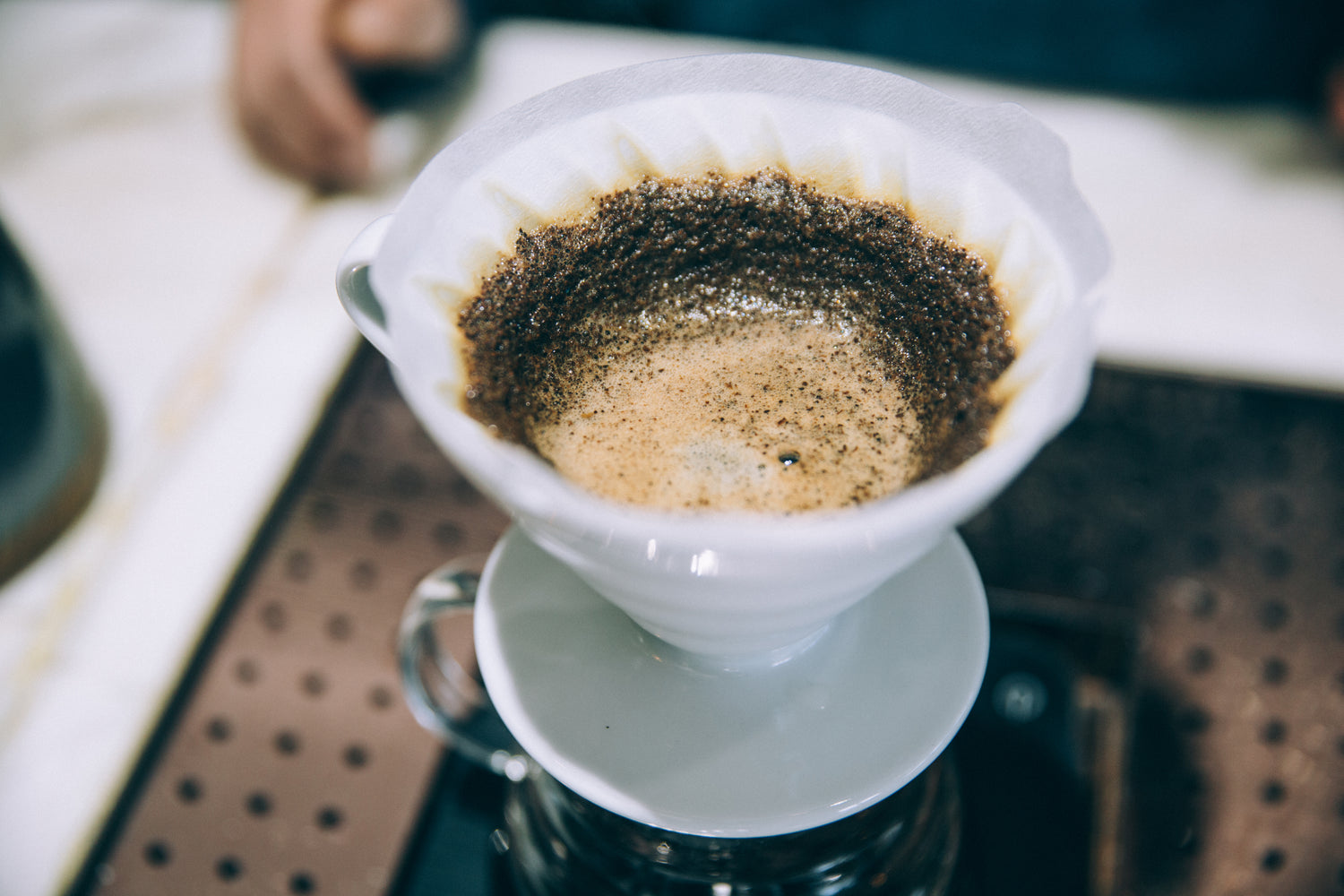 Image of a pour-over coffee setup, featuring hot water being poured over freshly ground coffee in a dripper placed on top of a glass carafe, with steam rising and a cozy kitchen setting in the background.